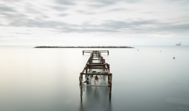 Seascape with old deserted industrial jetty at sunset. Abandoned damaged pier in the ocean. Long