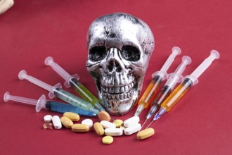 Composition of skull with syringes and pills on red background. Death from drug overdose concept