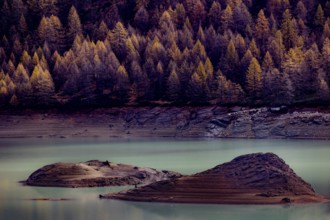 Two small islands in a lake surrounded by autumn trees with a calm water surface, Lago di Devero