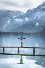 Girl with her arms open, standing on a narrow wooden deck, enjoying the view of the Austrian Alps