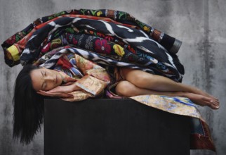 Sleeping beautiful woman lying on a black cube and covered by colorful blankets