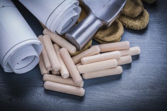 Close up view rolled blueprints hammer gloves wooden dowels