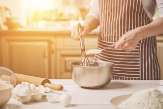 Young woman holding bowl with dough and whisk, closeup. A woman in a striped apron is cooking in