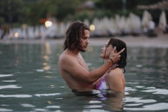 An intimate embrace between a couple in the ocean near the beach during the evening