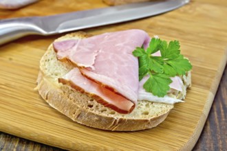 Bread with a slice of smoked ham and a sprig of parsley, knife on a wooden boards background