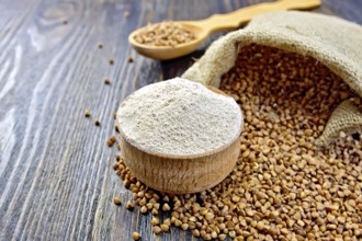 Buckwheat flour in a wooden bowl, buckwheat in a bag on a wooden boards background
