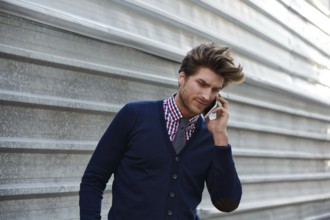 Young businessman talking smartphone phone on the street metal fence