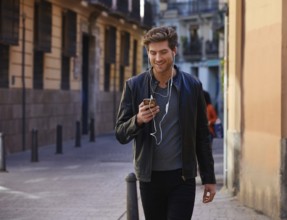 Young man listening music with smartphone earphones walking in the street