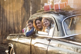 Overjoyed mother, father and little daughter looking out from window of car with Christmas presents