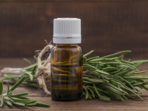 Rosemary essential oil in dark glass bottle and fresh rosemary on dark wooden background with copy