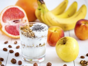 Healthy breakfast: yogurt with muesli and chia seeds, fruits and nuts on white wooden background.
