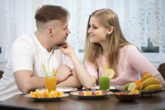 On a wooden table stand plates with various fruits. At the table sits a young couple. The man and