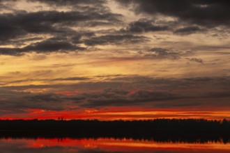 The stunning sunset showcases vibrant colors reflected on calm water, with dark silhouettes in the