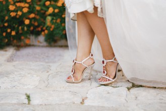 Bride's legs in stylish sandals with crystals with high heels peek out from under the wedding