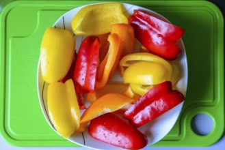Slices of bell peppers in a white plate on the green plastic board
