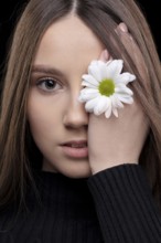 A beautiful girl with natural beauty holds a white flower near her eye. Young girl with a white