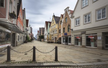 An empty shopping street with historic buildings and shop fronts under a cloudy sky, pedestrian