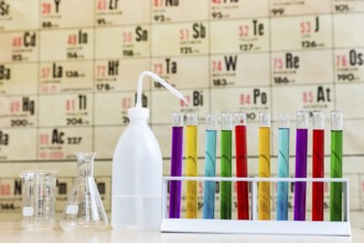 Chemistry with colored test tubes and glass in front of wallchart showing periodic table
