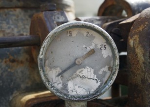 Old broken gauge with traces of numbers on the dial on a large old rusty engine