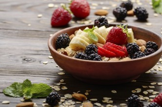 Fruit healthy muesli with banana strawberry almonds and blackberry in clay dish on wooden kitchen