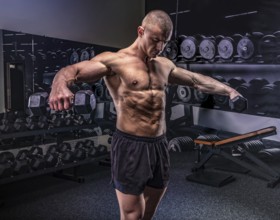 Young handsome sportsman lifting dumbbells in a gym