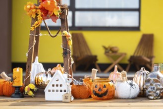 Autumn decor on porch of yellow house outside of pumpkin, lantern, garlands and figure of home and