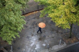 05.10.2023, Berlin, Germany, Europe, A person with an umbrella walks along a wet street in the