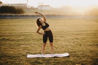 Woman performing a side stretch on a yoga mat in the open field