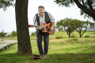 Musician looking at camera while playing guitar and singing in a park