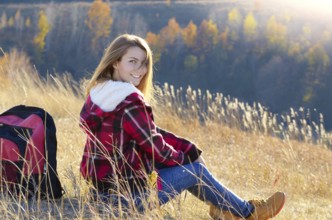 Young happy woman having fun outdoors sitting on the top of the hill. Backpacking tourism concept