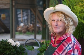 Side head-and-shoulders portrait of a middle-aged blonde woman with straw hat and gardener's apron