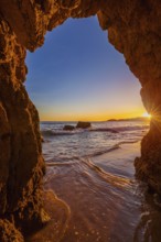 View from the beach through a rock formation to the Atlantic Ocean, sunset on the Algarve coast,