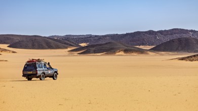 An off-road vehicle stands in vast sand dunes under a clear, sunny sky, off-road through the