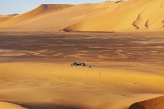 Wide sand dune landscape in yellow tones, with a small camp in the middle of the dunes, tent camp