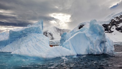 Large icebergs in a cloudy sky with an opening in the background that lets sunlight through,