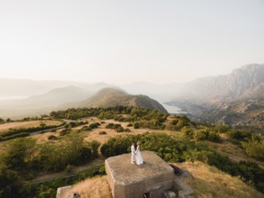 The bride and groom hold hands on the roof of the Gorazda fort, behind them a view of the Bay of