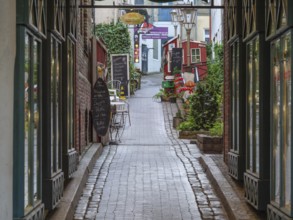 Narrow cobbled alley with old buildings and alleyway café in a cosy atmosphere, Flensburg,