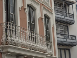 Detailed view of an old building façade with ornate balconies and windows. The colours are muted,