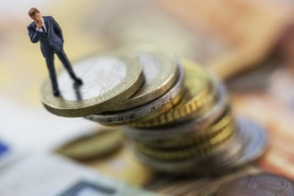 Figure of a thoughtful businessman between euro coins, studio shot, Germany, Europe