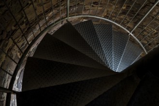 Steps of old metal spiral staircase disappear in darkness