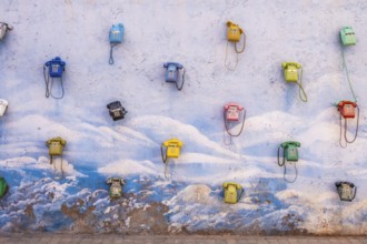 Colored telephones hanging in a blue and white wall. Urban art in the middle of nowhere