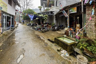 A narrow, wet road in a provincial area with parked motorbikes and colourful flags, road through a