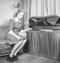 Woman at a gramophone in the 1940s. She has put a record on and is listening to the music. The
