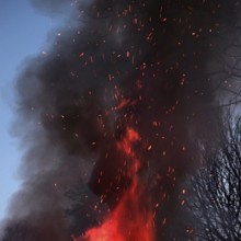 Crackling flames eat into the high pile of an Easter fire, dark smoke with flying sparks rises and