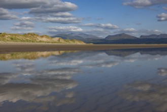 Reflection of clouds and mountains of Snowdonia National Park in the water on the beach,