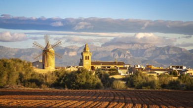Cosy village with windmill and church and mountains in the background under a cloudy sky, Algaida,