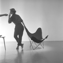 Home decor of the 1950s. A young woman is standing beside the popular Butterfly chair, also known