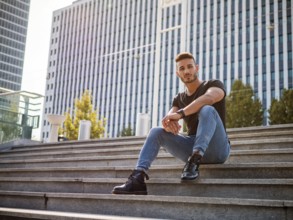 One handsome young man in urban setting in European city, wearing jeans and black t-shirt