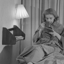 Teatime in the 1950s. A young woman in an evening gown sits comfortably and drinks a cup of tea.