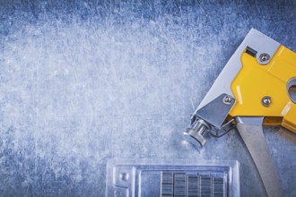 Yellow tacker stapler gun chrome staples on scratched metallic background